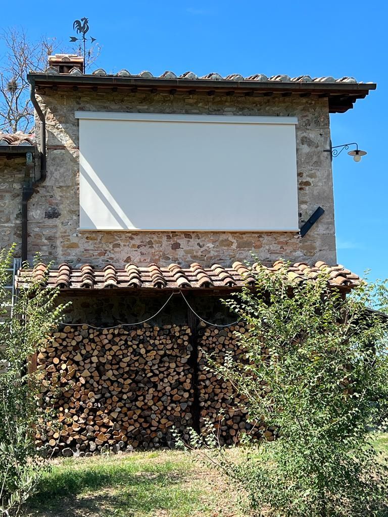 Vecchia casa in pietra con un grande pannello bianco vuoto sopra una catasta di legna e della vegetazione davanti.