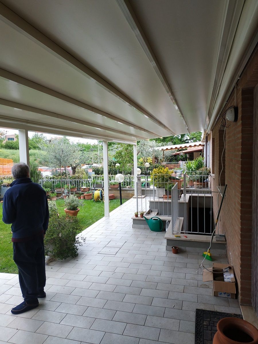 Un patio coperto con piante in vaso, un uomo in piedi sulla sinistra e la facciata di una casa in mattoni.