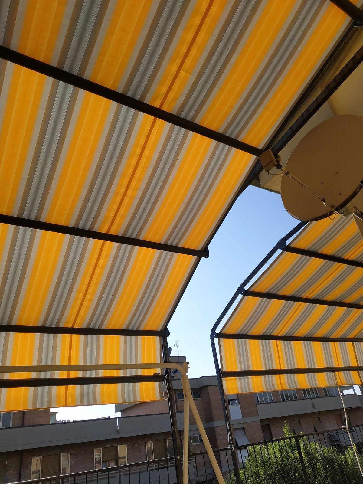 Tende a strisce gialle e bianche sopra un'area con posti a sedere all'aperto, con il cielo azzurro visibile sopra.