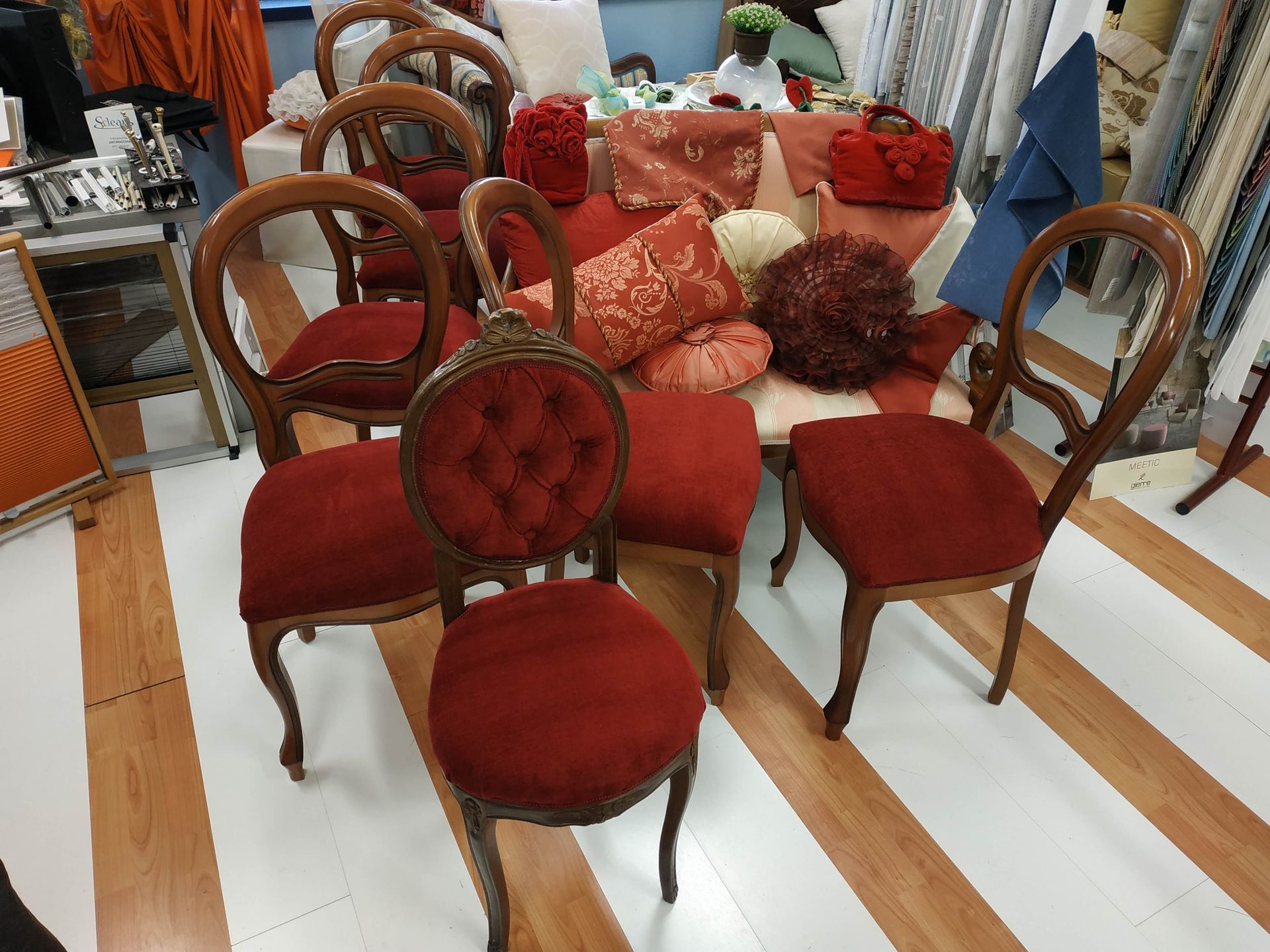 In uno showroom di mobili, quattro poltrone vintage in velluto rosso sono disposte intorno a un divano abbinato.