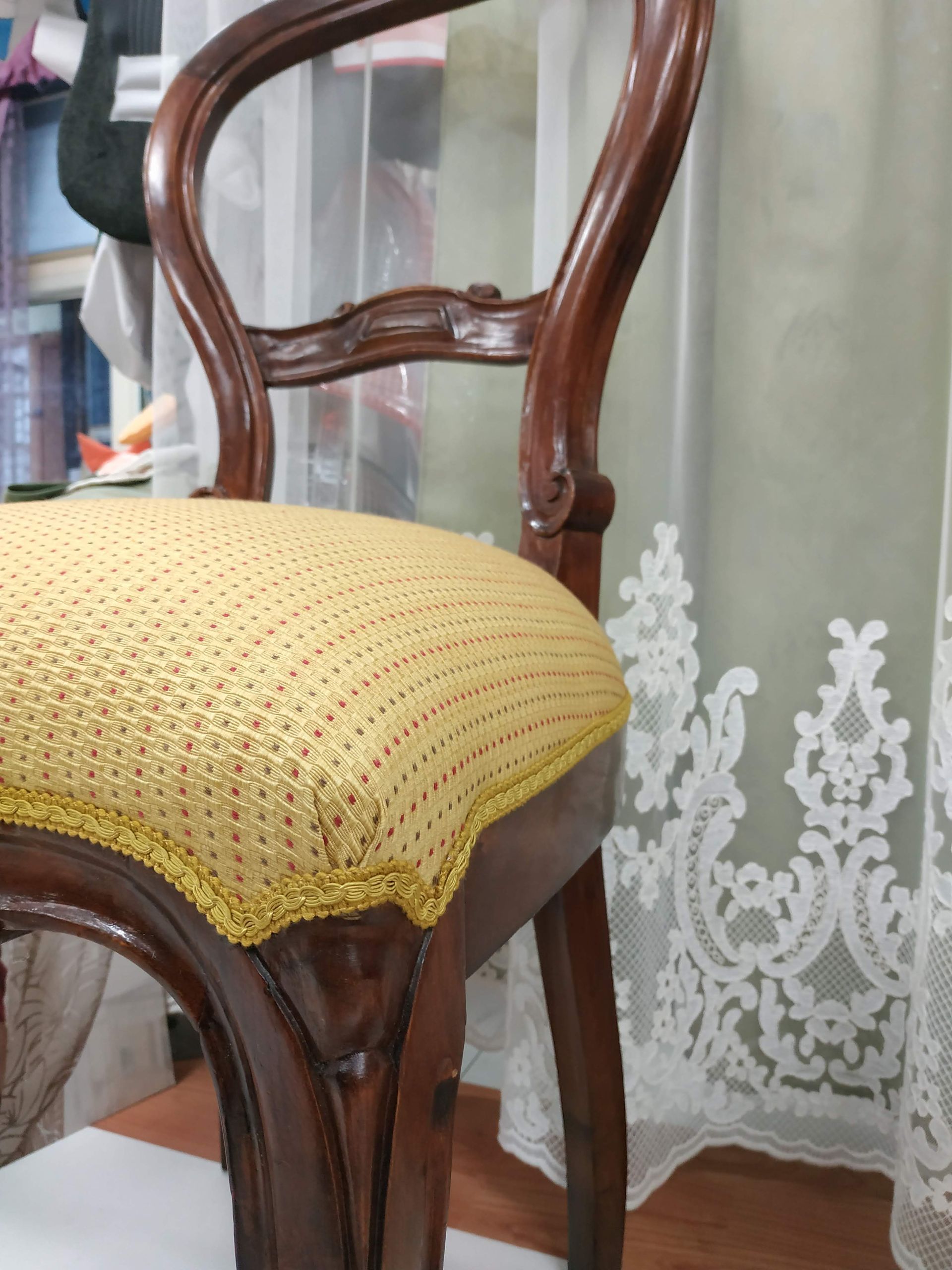 Sedia di legno con cuscino giallo all'uncinetto accanto a una tenda di pizzo su un pavimento in legno massello.