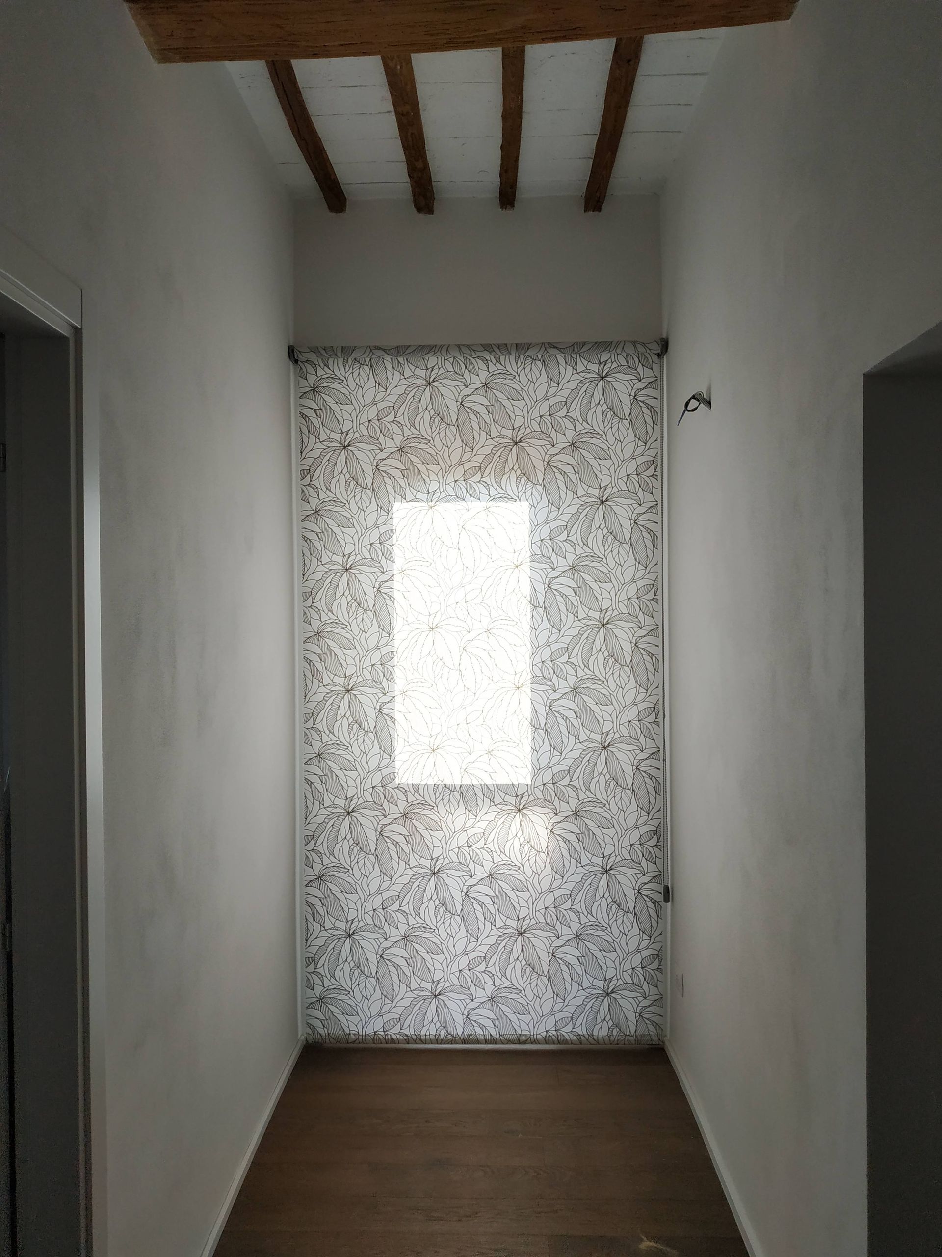 Stretto corridoio con pareti bianche, pavimento in legno, travi a vista sul soffitto e una porta in vetro smerigliato in fondo.