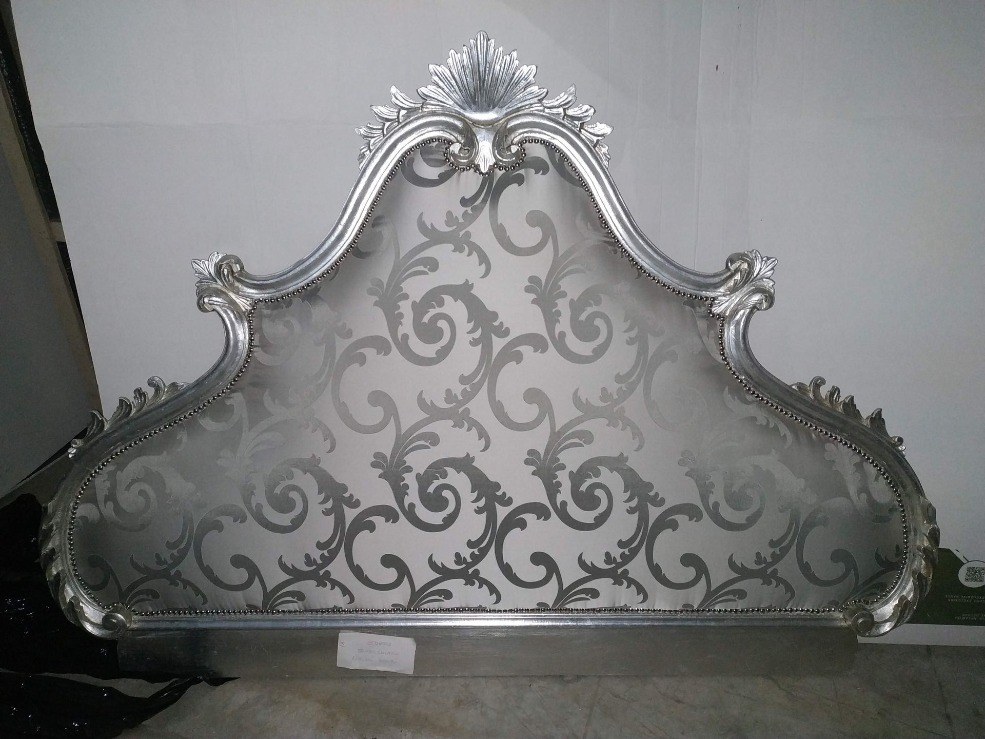 Paravento decorativo con cornice argentata e ornato motivo floreale a volute grigie.