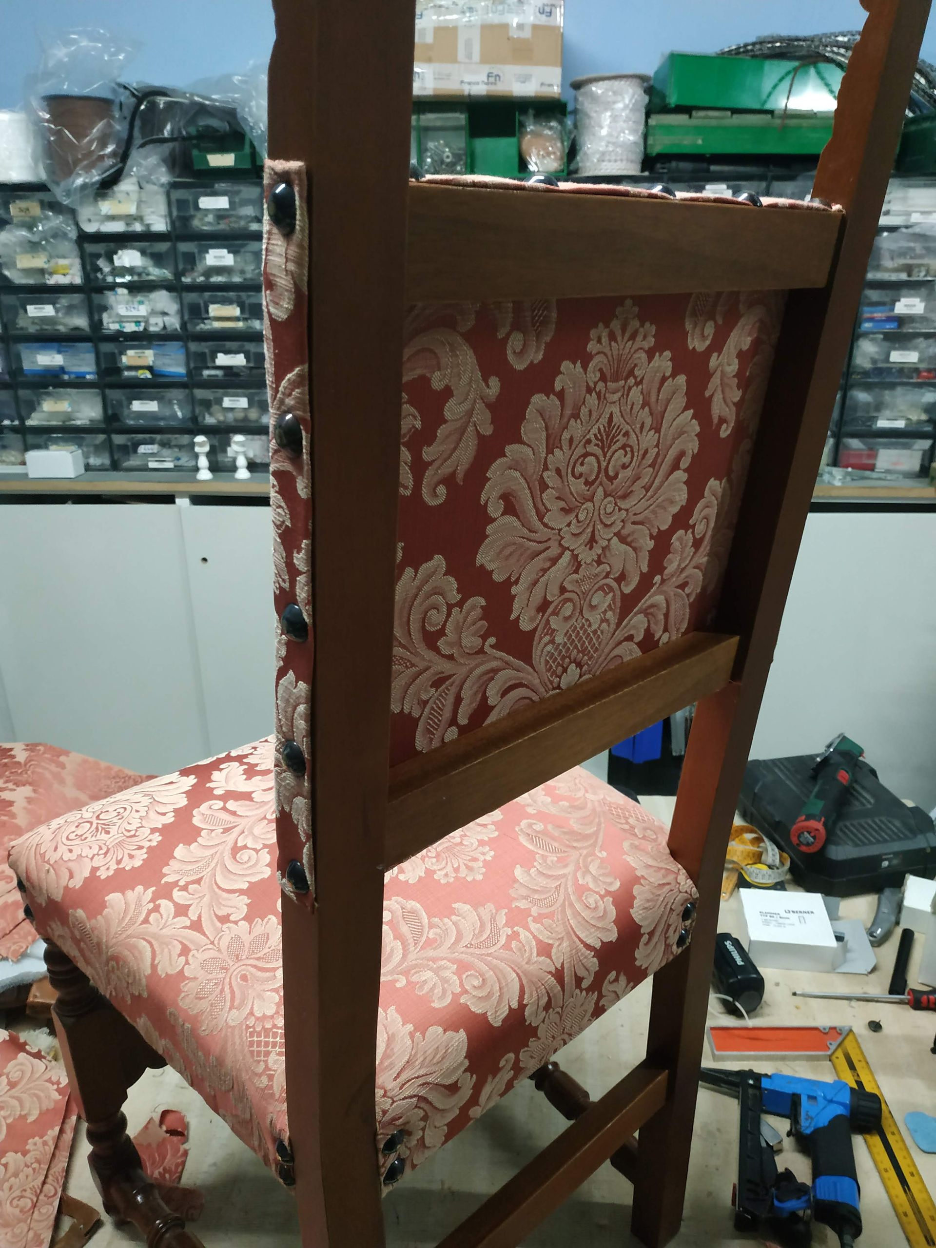 Sedia in legno imbottita di rosso in un'officina o in un negozio disordinato, vista da dietro.