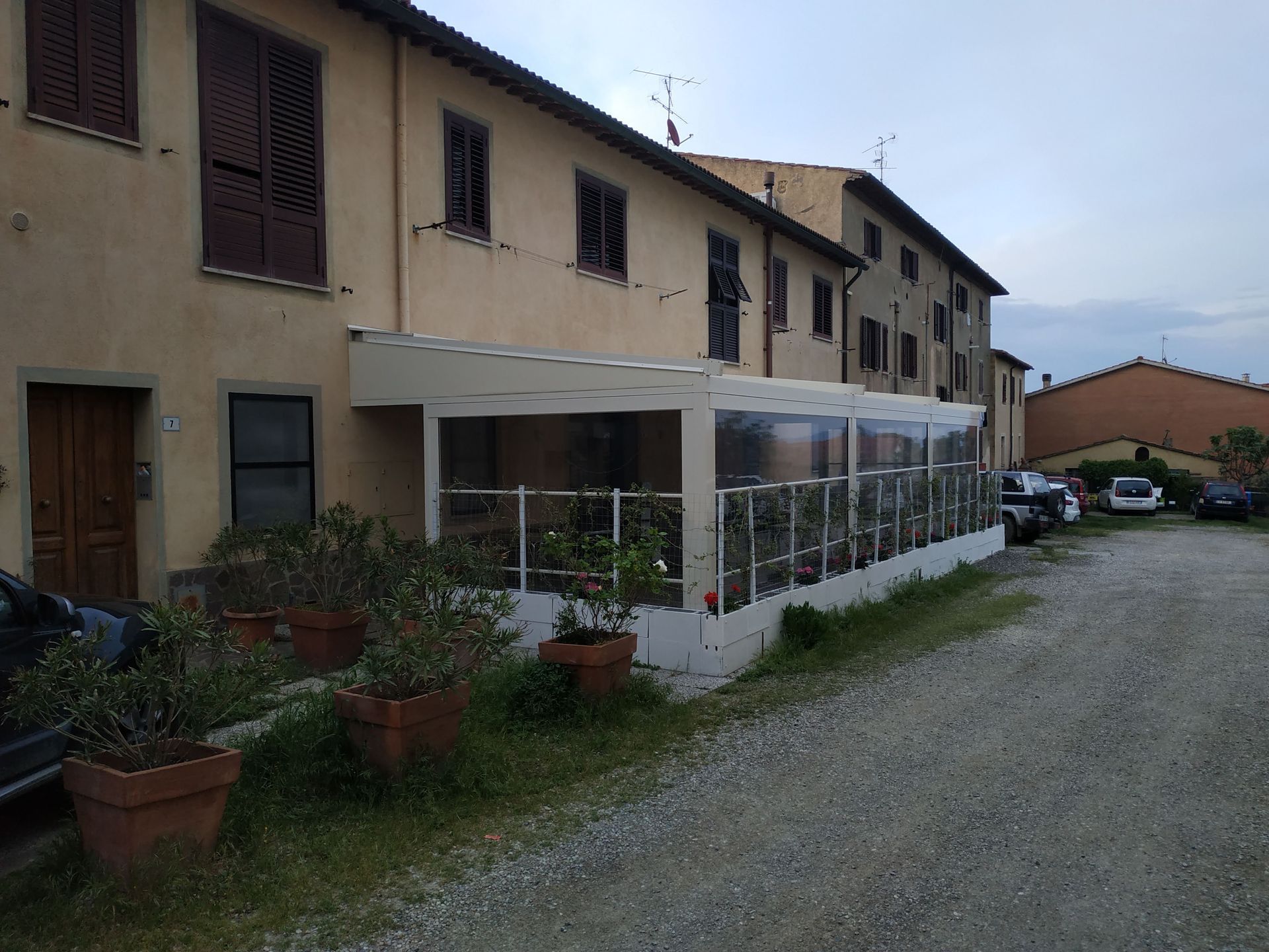 Fila di villette a schiera beige con patio coperto, piante in vaso e vialetto di ghiaia antistante.