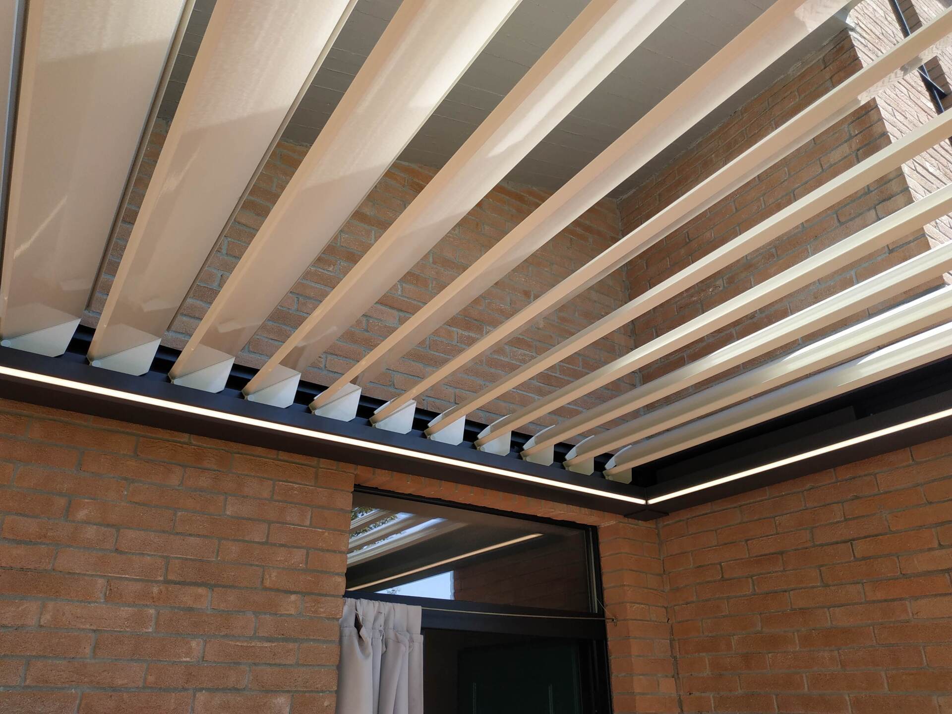 Passaggio esterno coperto con tettoia a pergola in listelli bianchi tra muri in mattoni