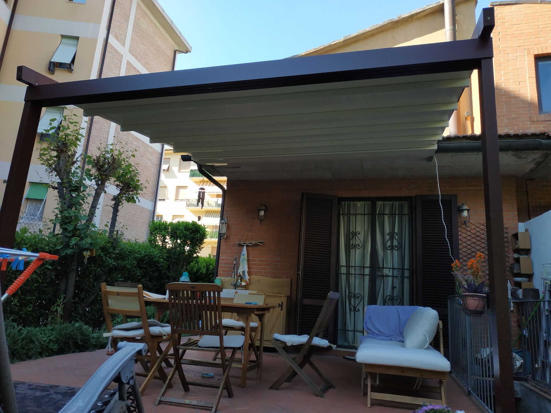 Patio posteriore con tenda da sole, tavolo e sedie e un divanetto imbottito accanto alle porte scorrevoli in vetro.