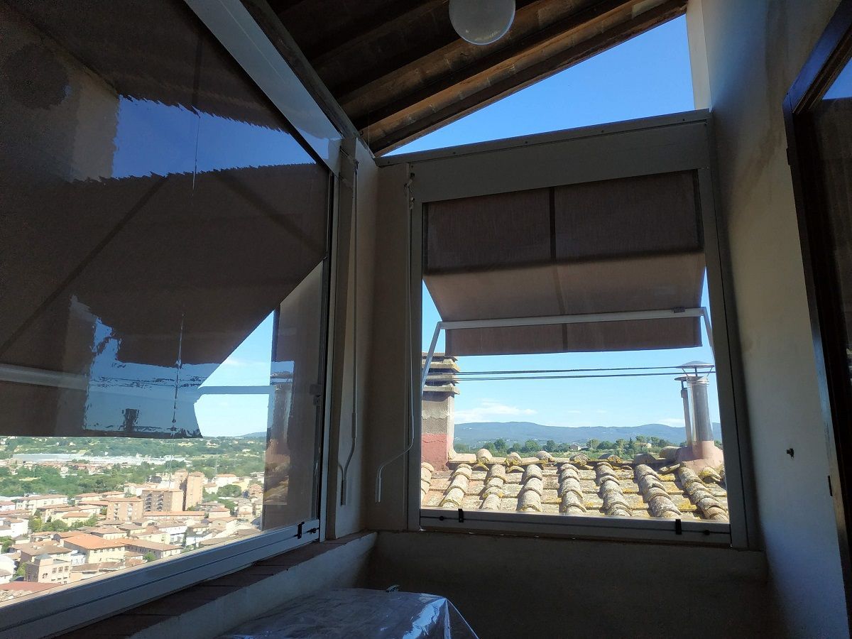 Vista interna da una finestra della veranda con vista su una cittadina costiera e sul mare blu sottostante.