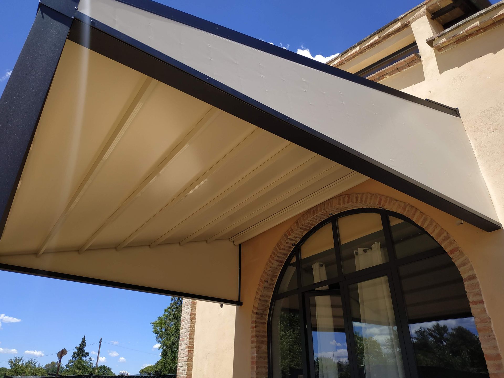 Tenda a righe beige sopra una finestra ad arco e un muro di mattoni sotto un cielo azzurro