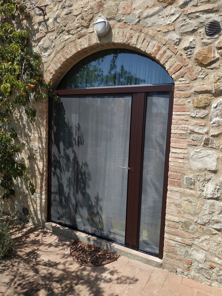 Muro in pietra con finestra o porta ad arco, coperto da un paravento grigio e finiture scure.