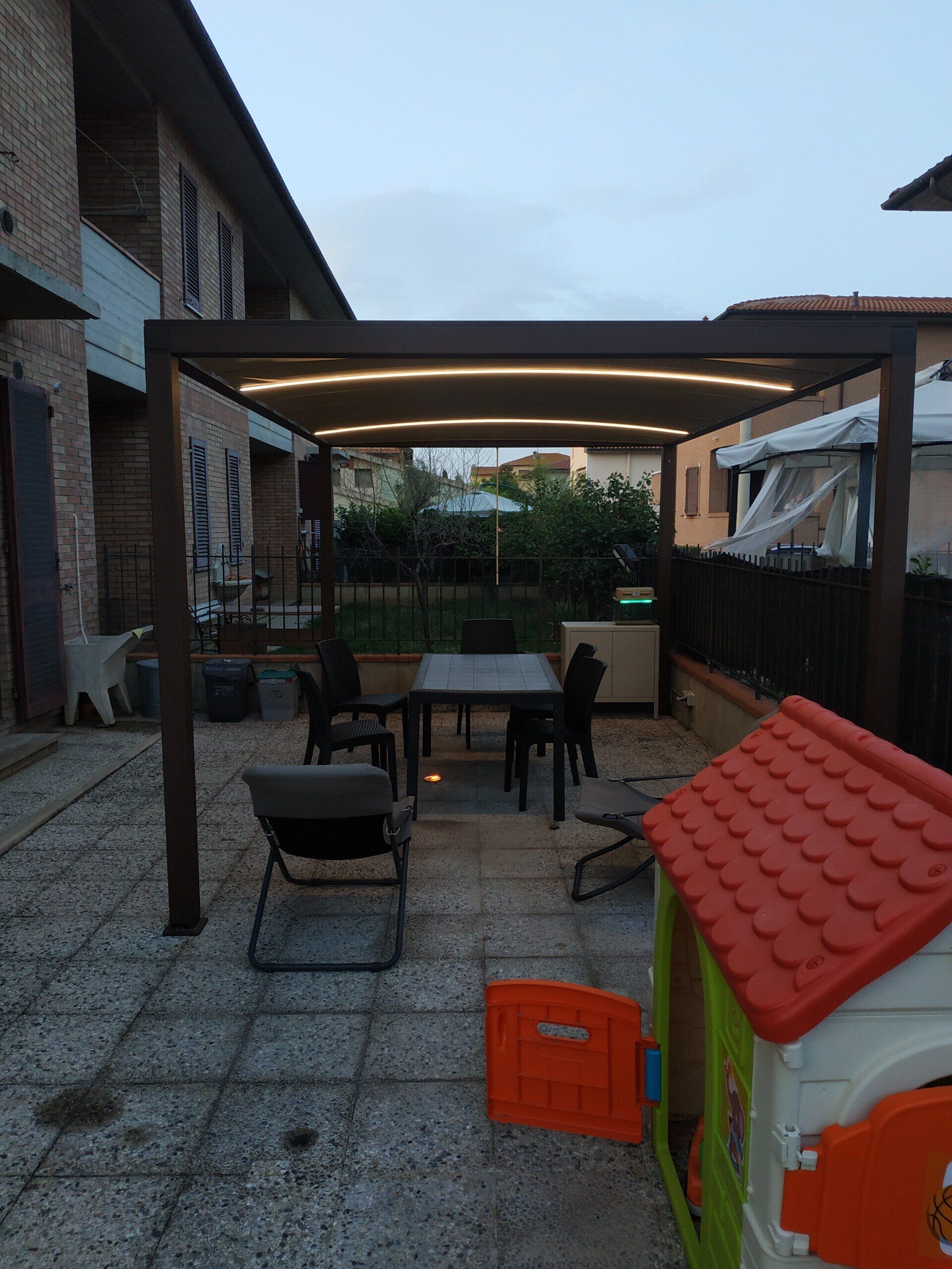 Patio sul retro con tavolo, sedie, pergolato e una piccola casetta per giocare al crepuscolo