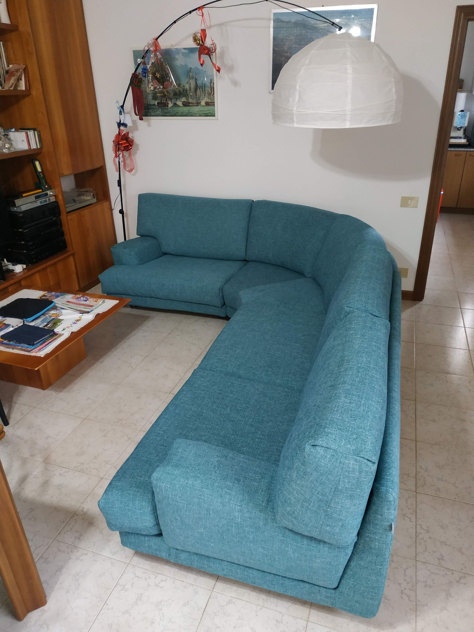 Divano angolare blu in un piccolo soggiorno con lampada bianca e tavolino da caffè.
