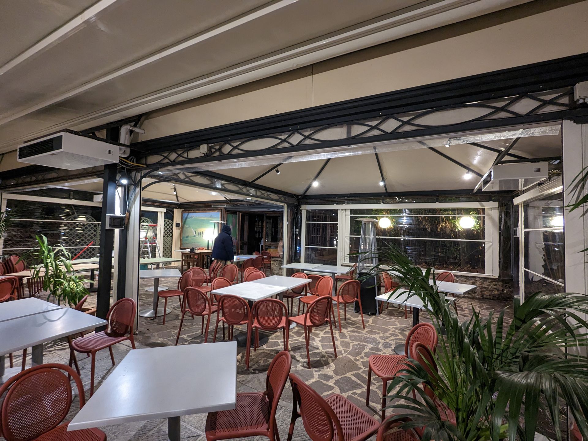 Caffè all'aperto coperto con tavoli bianchi, sedie rosse e piante di notte