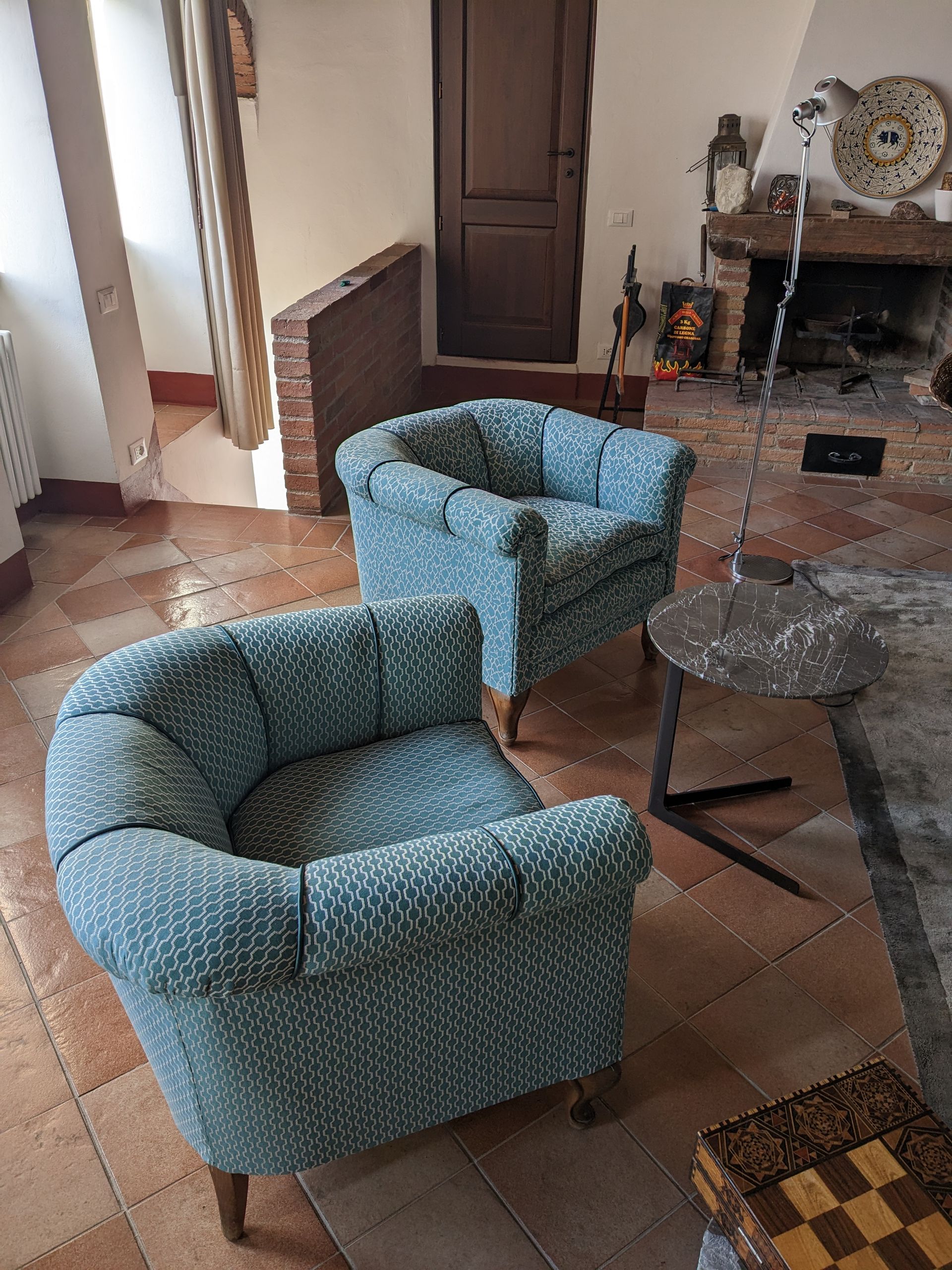 Accogliente soggiorno con due poltrone blu, un tavolino rotondo e un camino sullo sfondo.