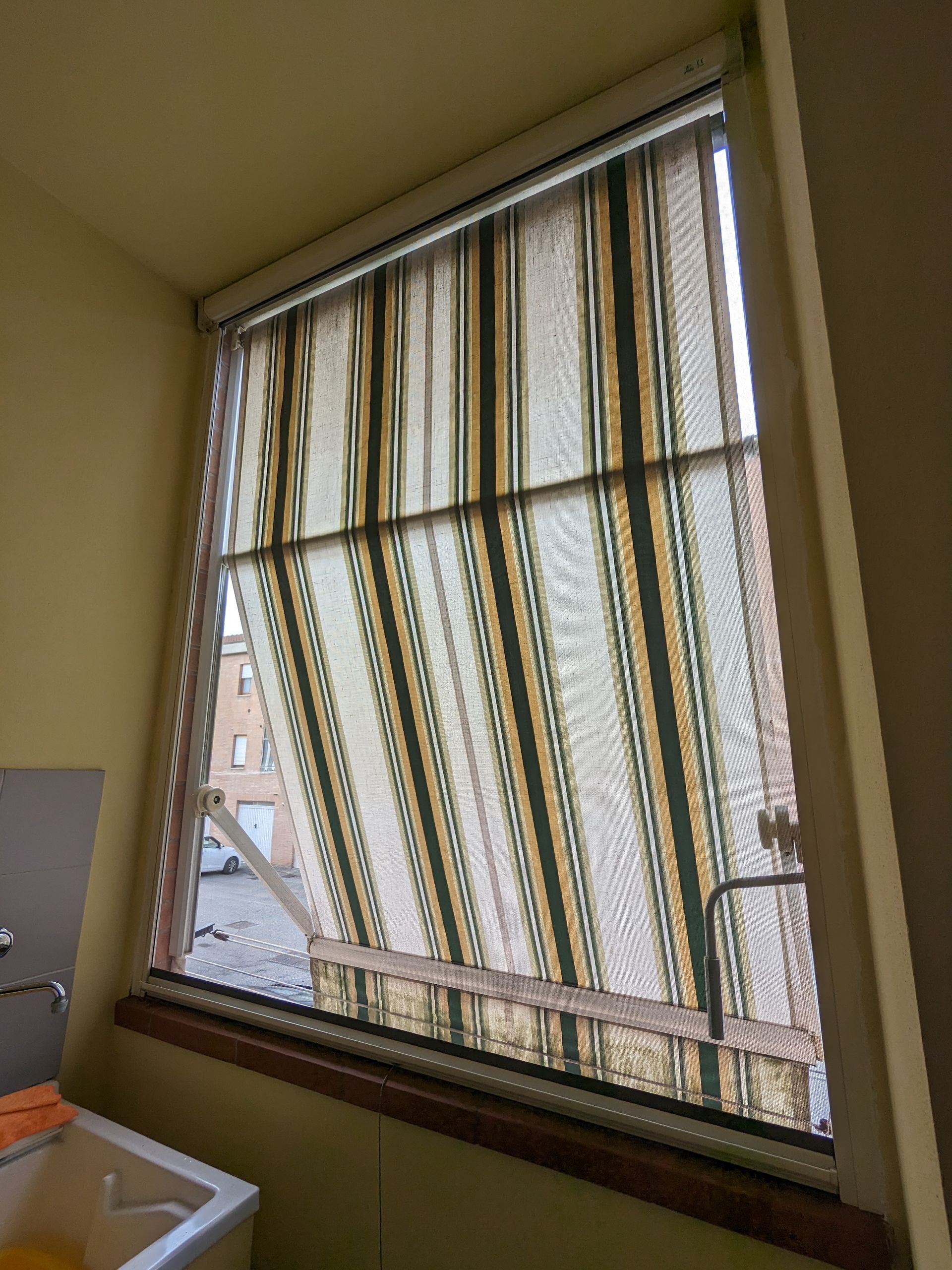Tenda a righe appesa in una stanza beige accanto a un lavandino e alla maniglia della porta.