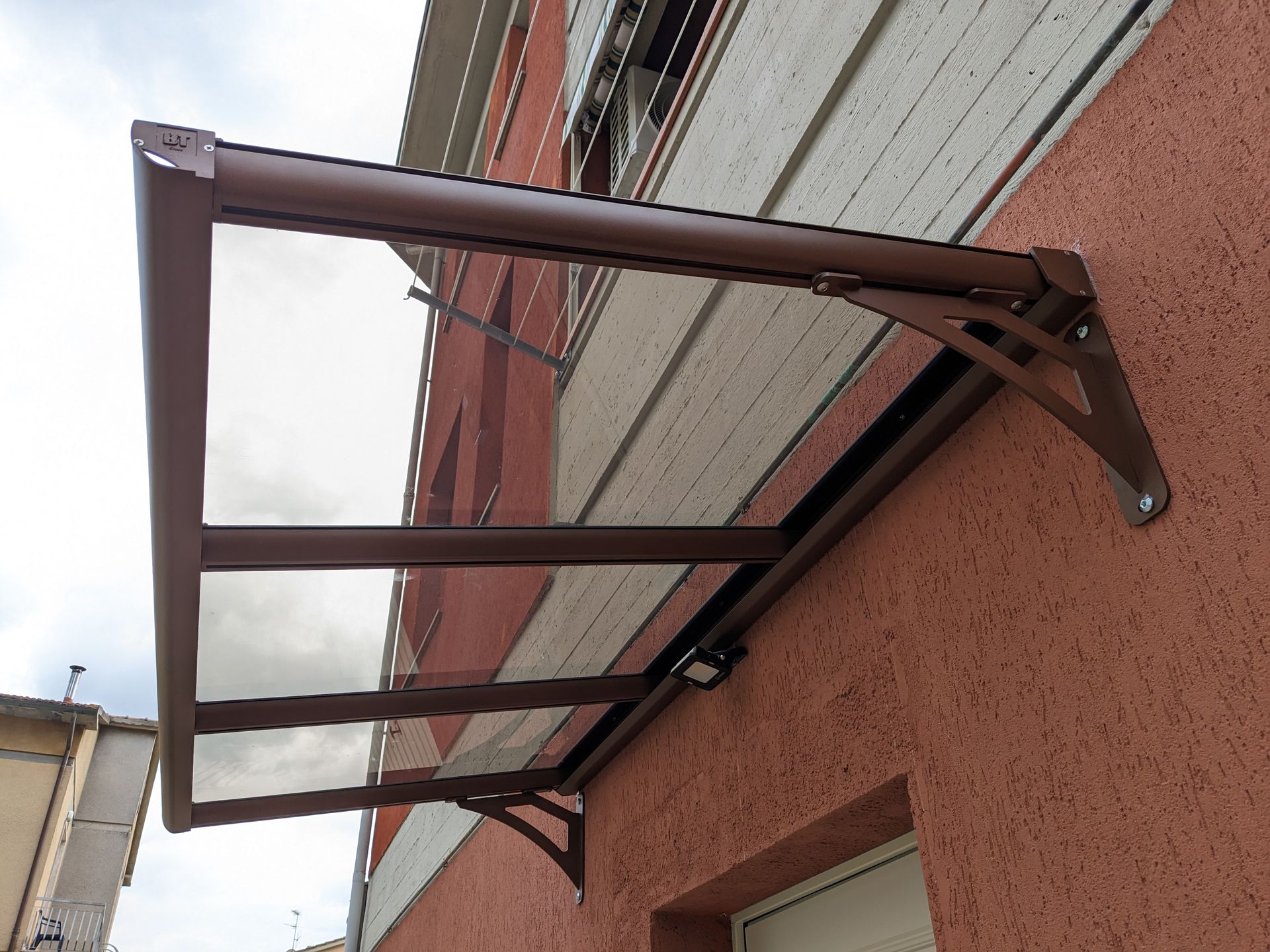 Supporti in metallo marrone per tenda da sole montati sopra una finestra di un edificio, visti dal basso.
