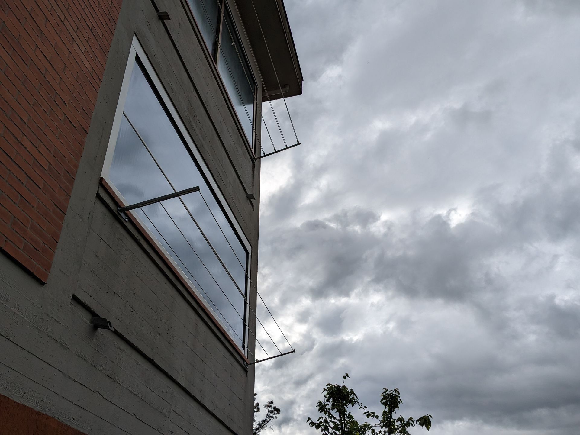Vista inclinata di un edificio in mattoni con finestre contro un cielo grigio e nuvoloso, con le cime degli alberi sottostanti.