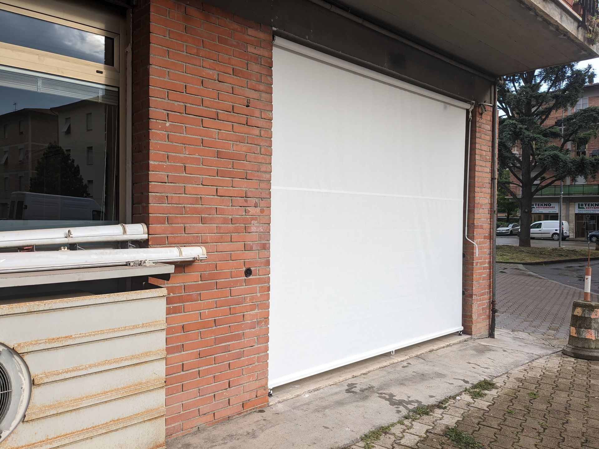Porta da garage bianca incastonata in un edificio in mattoni accanto a un marciapiede e a una strada.