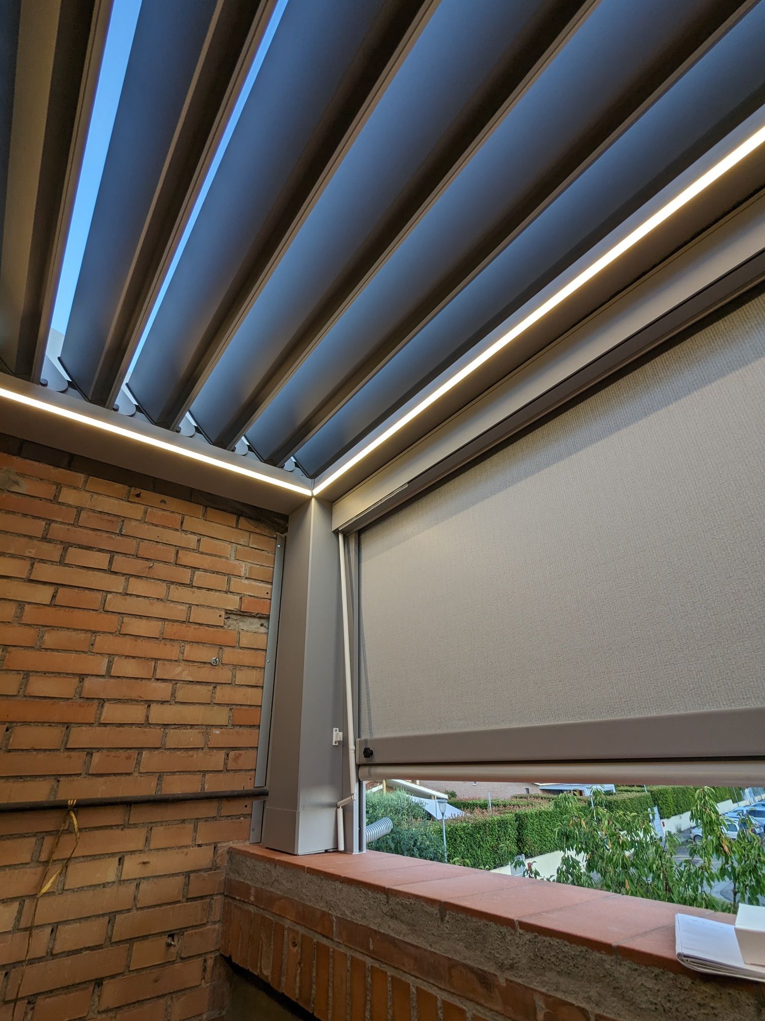 Balcone esterno con muro in mattoni, tenda da sole retrattile e telo parasole grigio parzialmente abbassato.