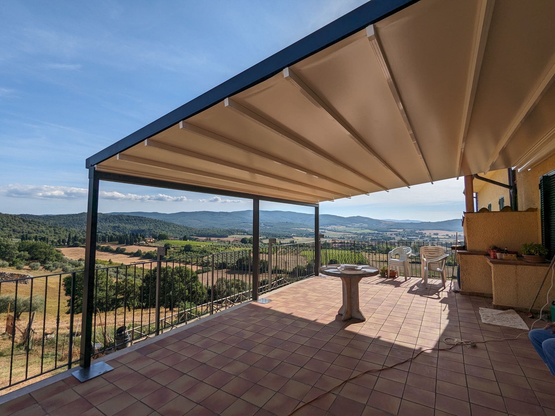 Terrazza coperta con pavimento piastrellato, tavolo e sedie, affacciata su una valle soleggiata e sulle colline in lontananza.