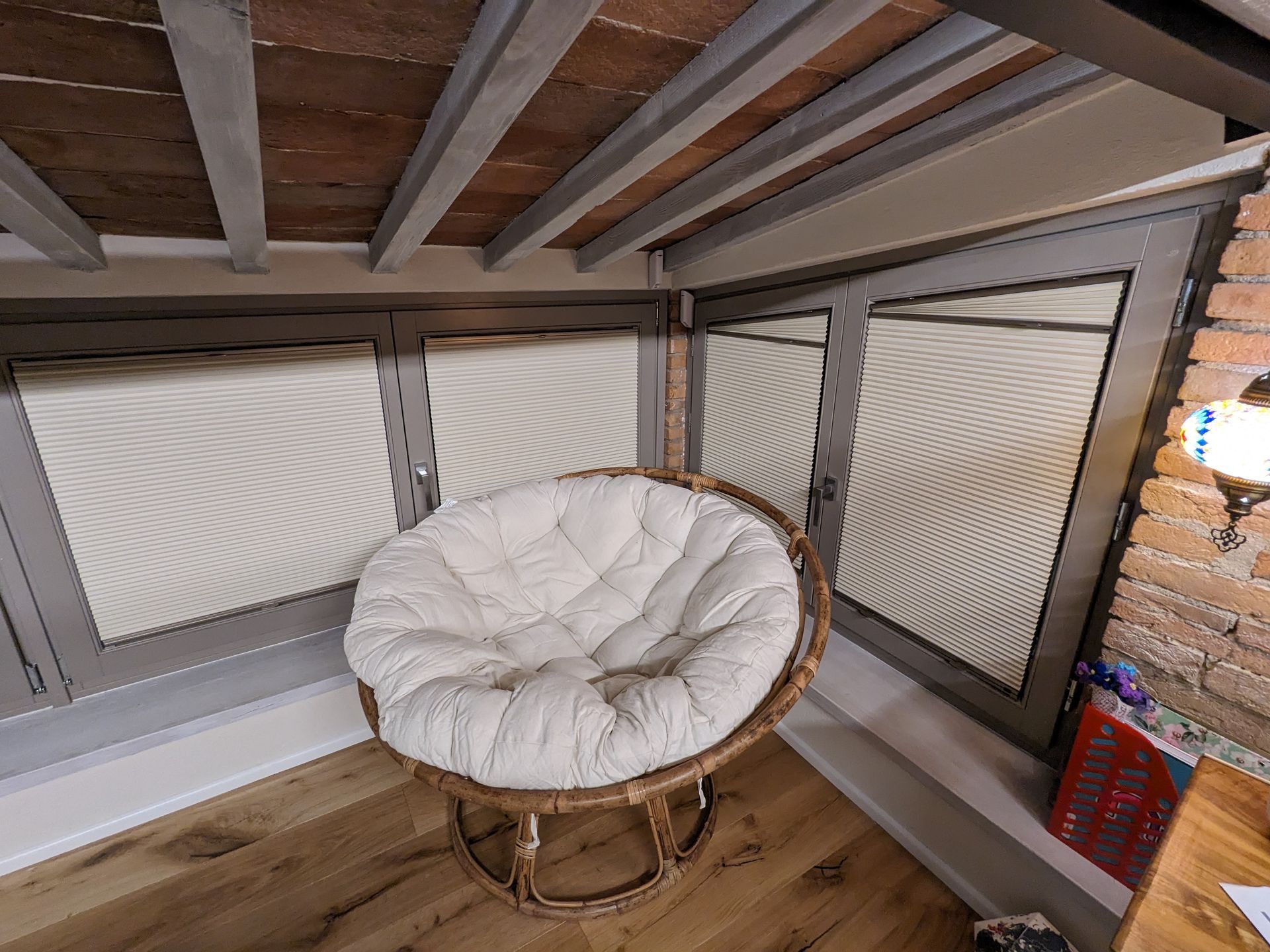 Accogliente poltrona in vimini con cuscino bianco in un angolo del loft sotto un soffitto inclinato in legno.