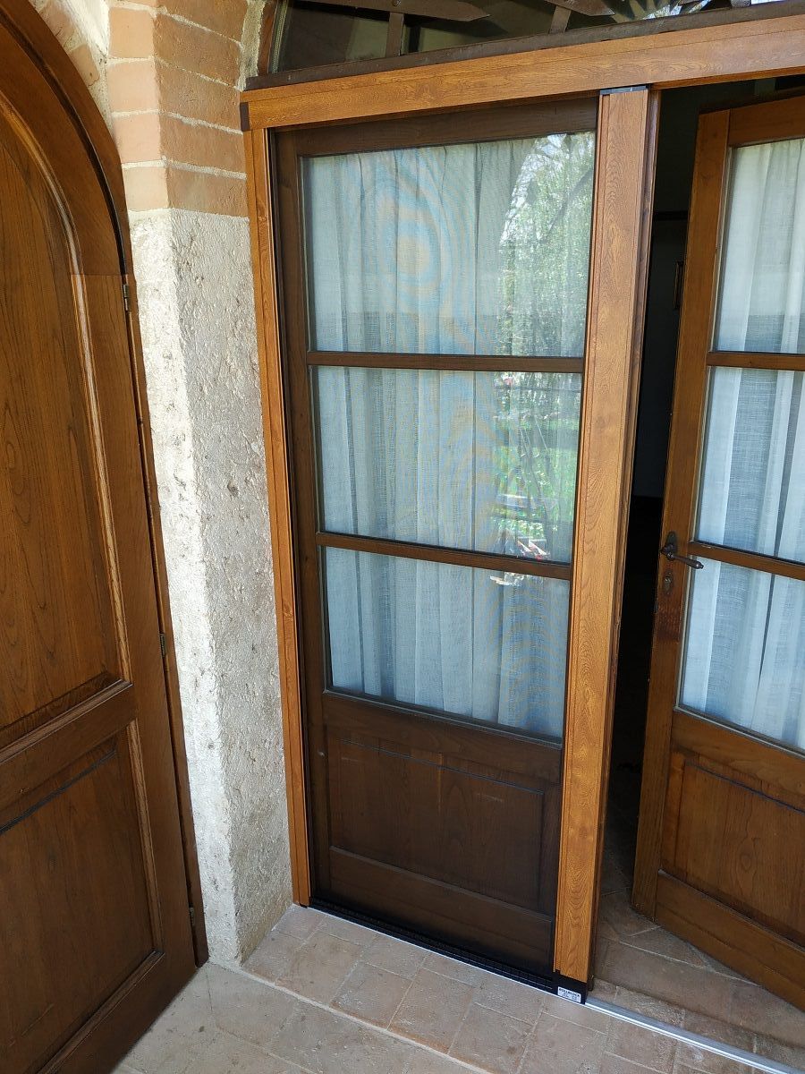 Porte a vetri con telaio in legno e tende trasparenti accanto a un muro di mattoni e pannelli in legno.