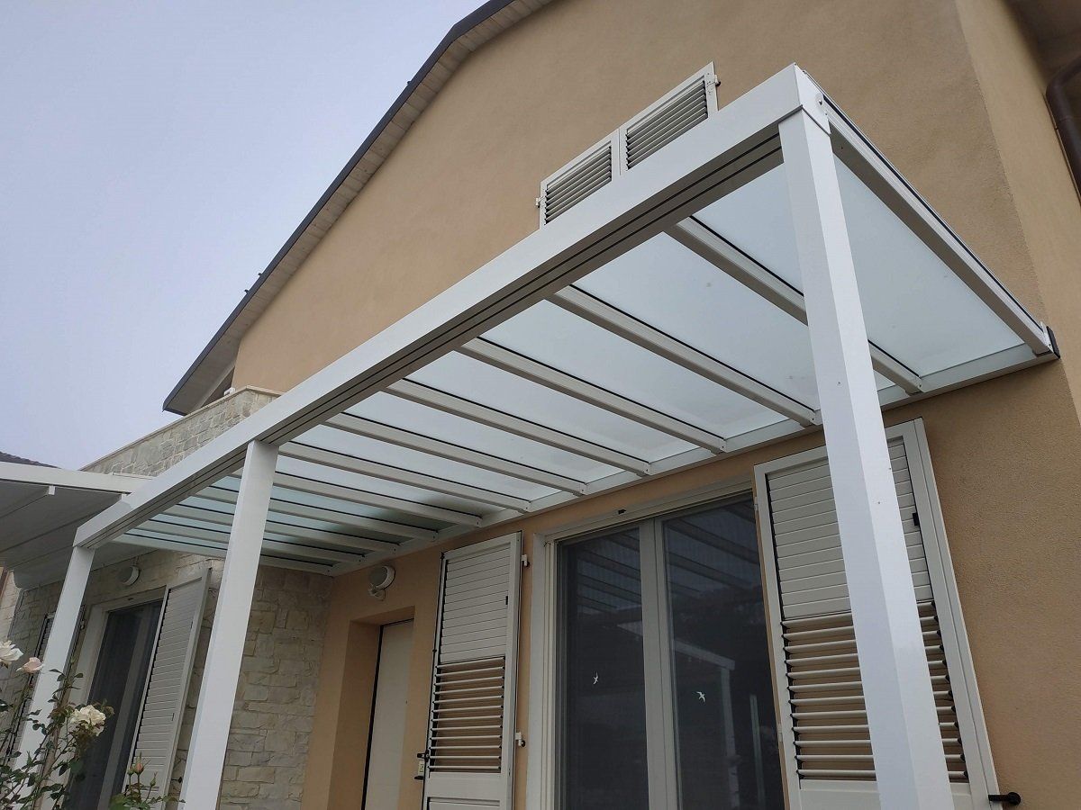 Tenda da sole in metallo bianco sopra l'ingresso di una casa con finestre a persiana e muro in stucco color beige.