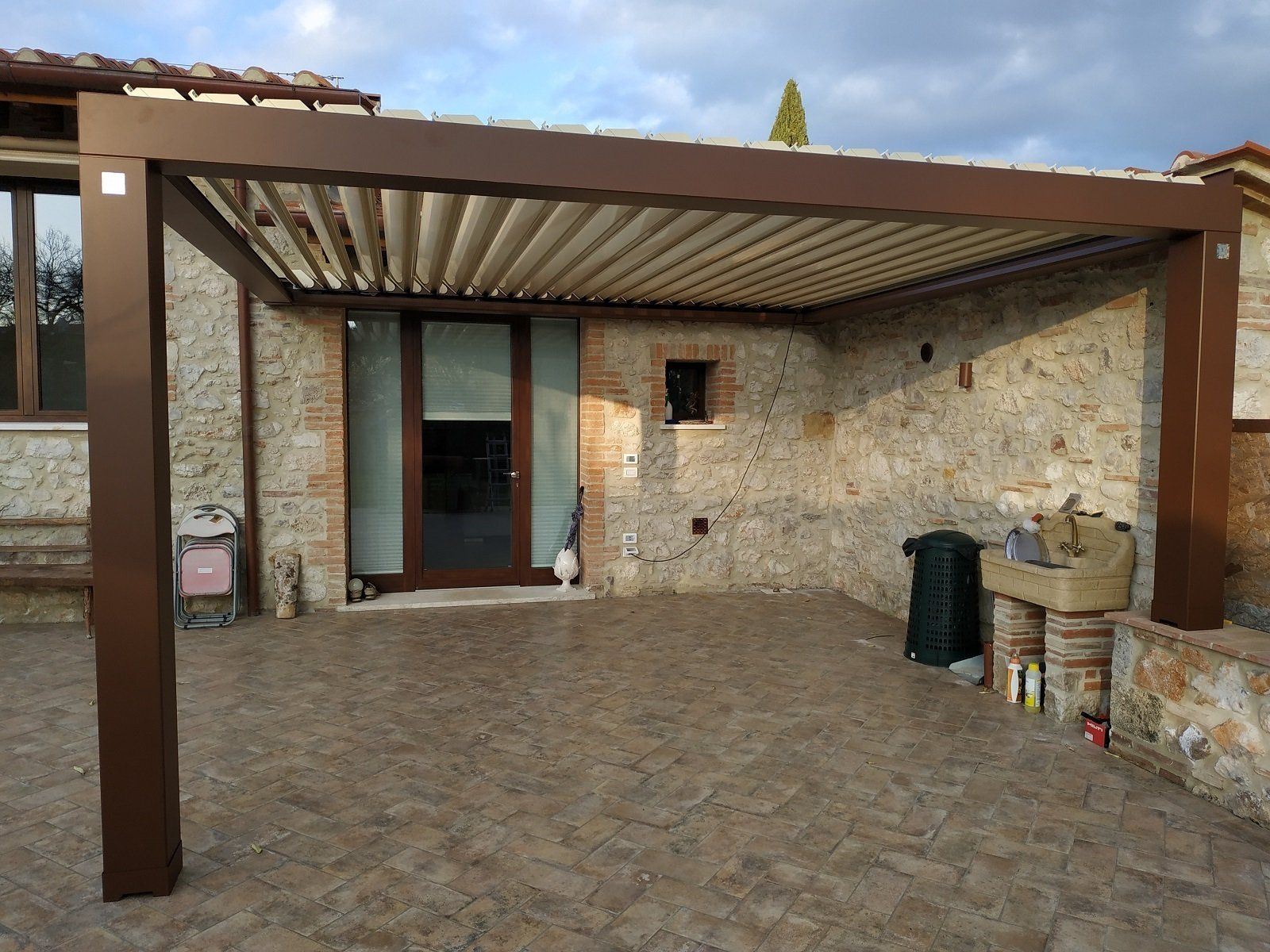 Patio coperto con muri in pietra, pavimento piastrellato e tettoia in legno.
