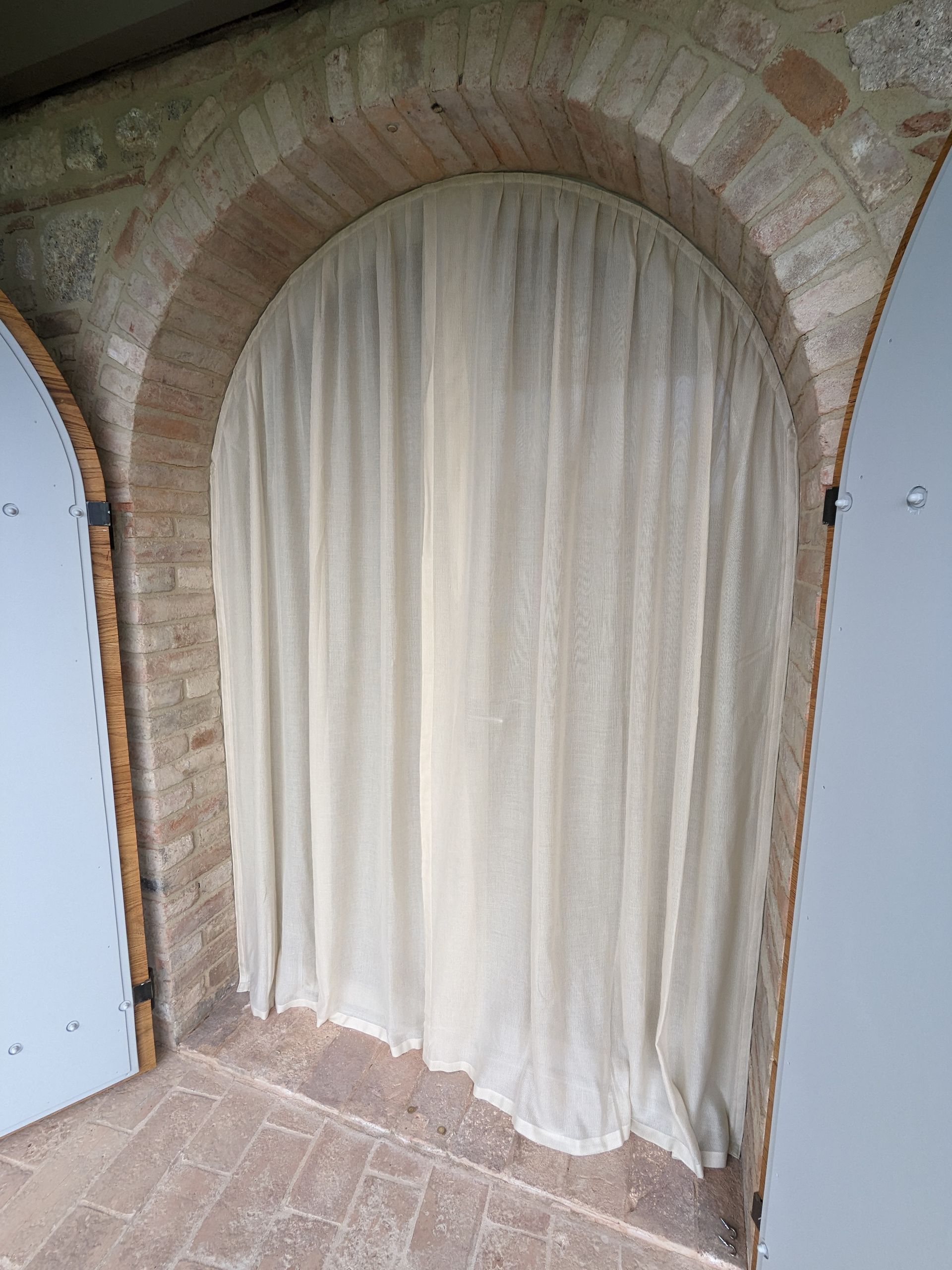 Portale ad arco in pietra con tenda color crema che pende sopra l'ingresso su un pavimento piastrellato.