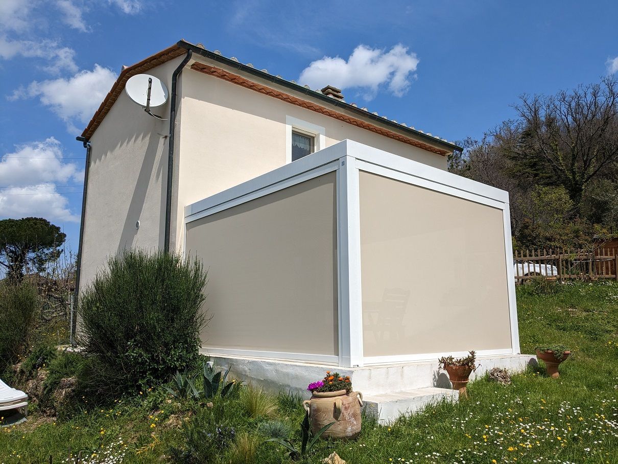 Casa con veranda chiusa beige e finiture grigie su una collina erbosa sotto un cielo azzurro