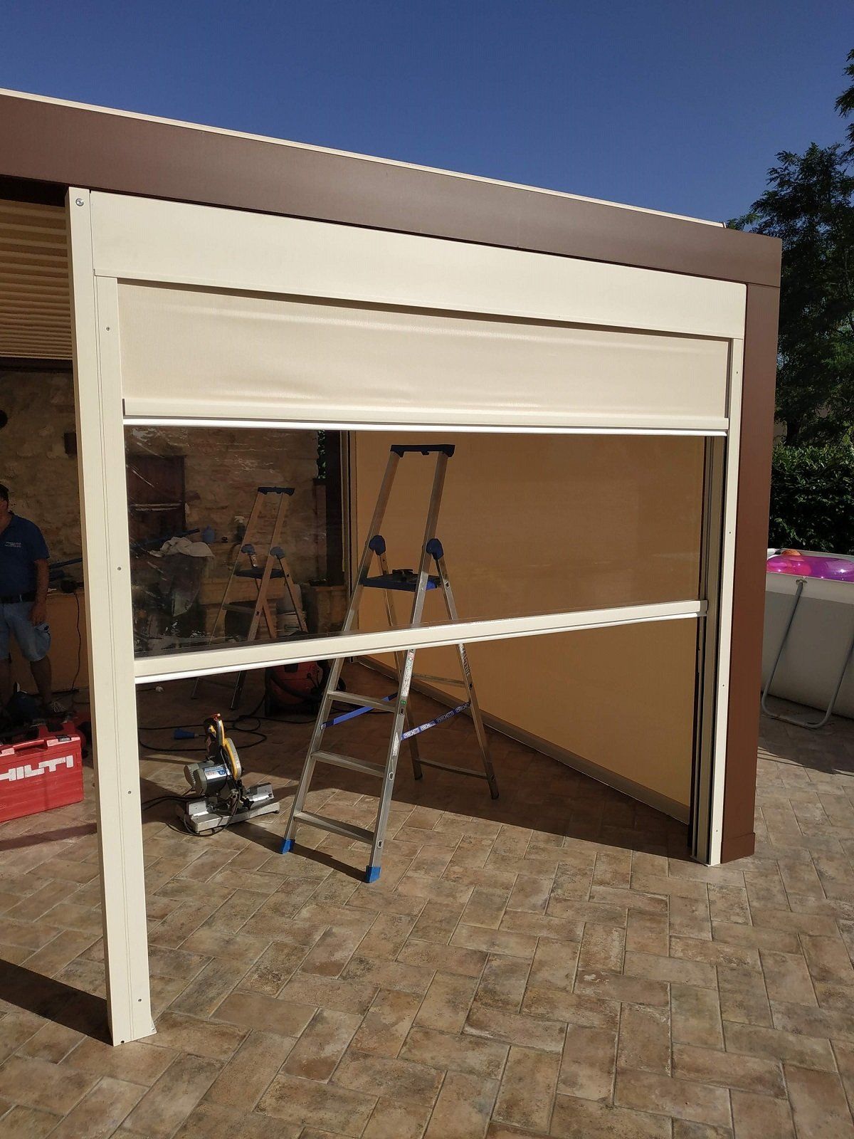 Struttura di tenda da sole bianca per vetrina in fase di costruzione, con scale e attrezzi in un'area piastrellata del patio.