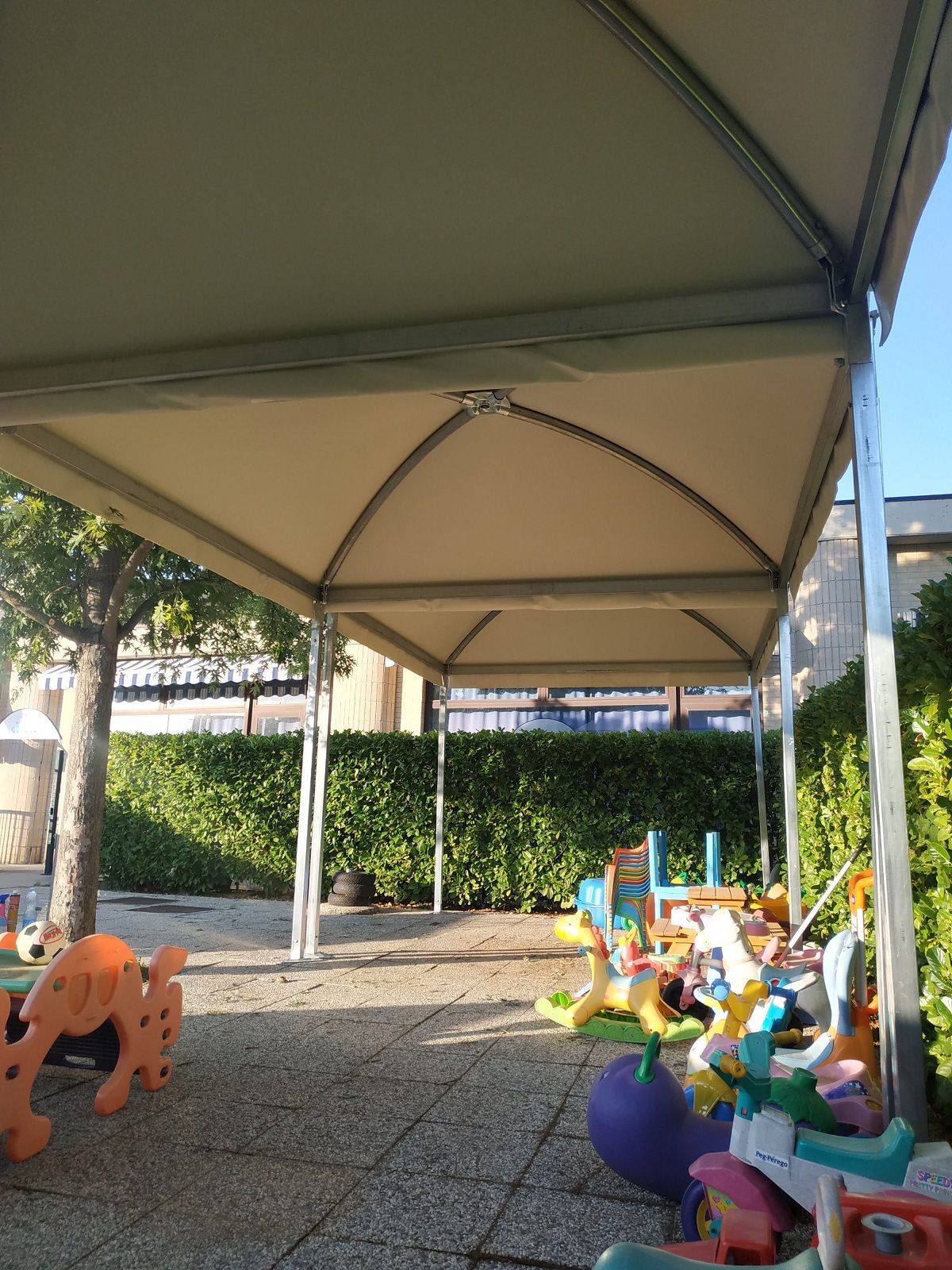 Parco giochi sotto un'ampia tettoia con colorati giochi cavalcabili e una superficie di ghiaia.