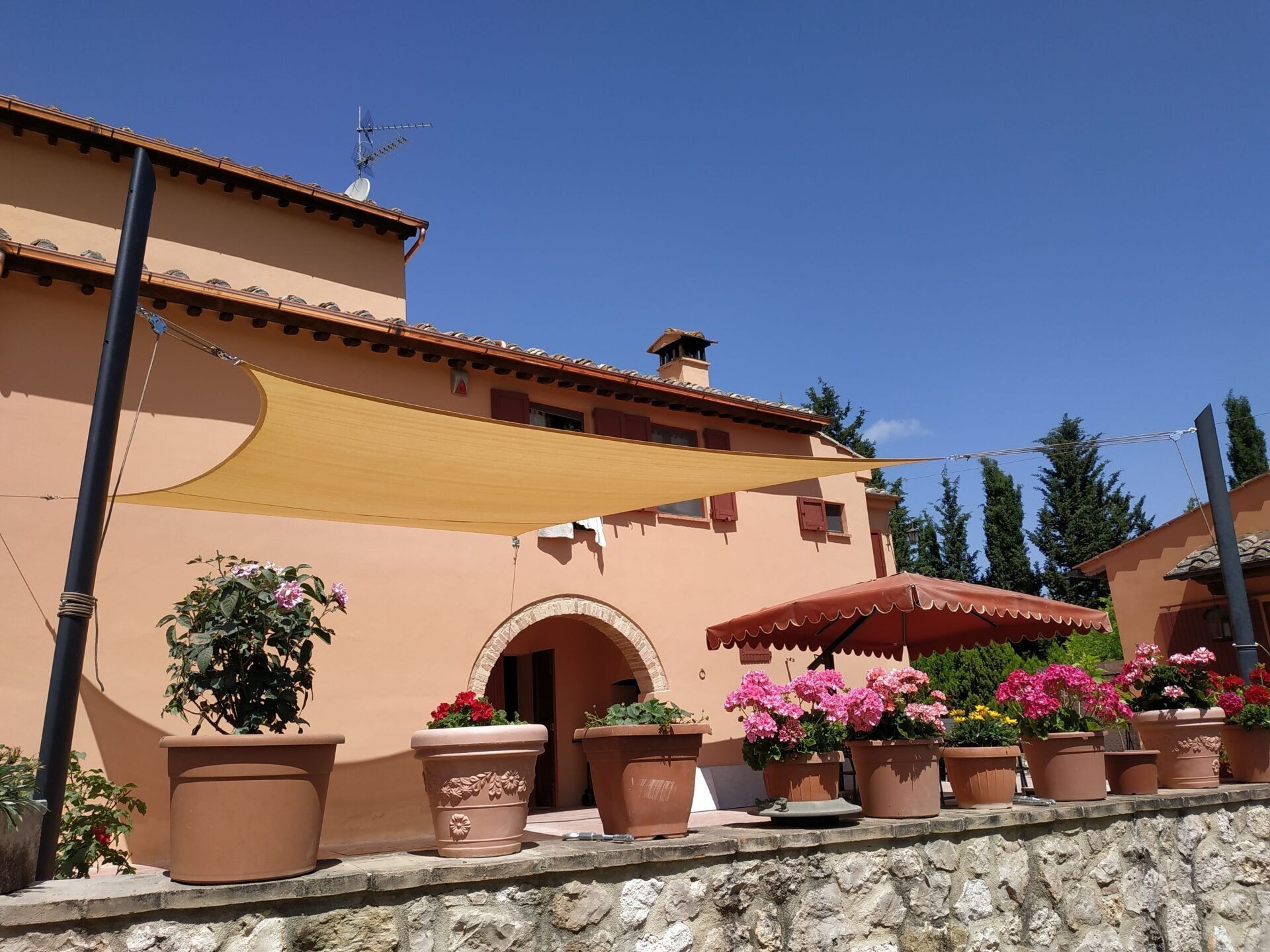 Casa in stile mediterraneo, soleggiata, con tetto in terracotta e vasi di fiori rosa lungo un muro di pietra.