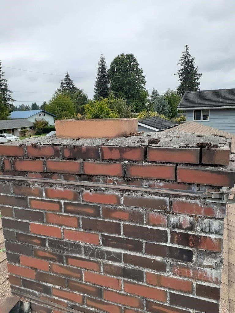 Damaged brick wall with missing top bricks and a concrete cap in a residential yard