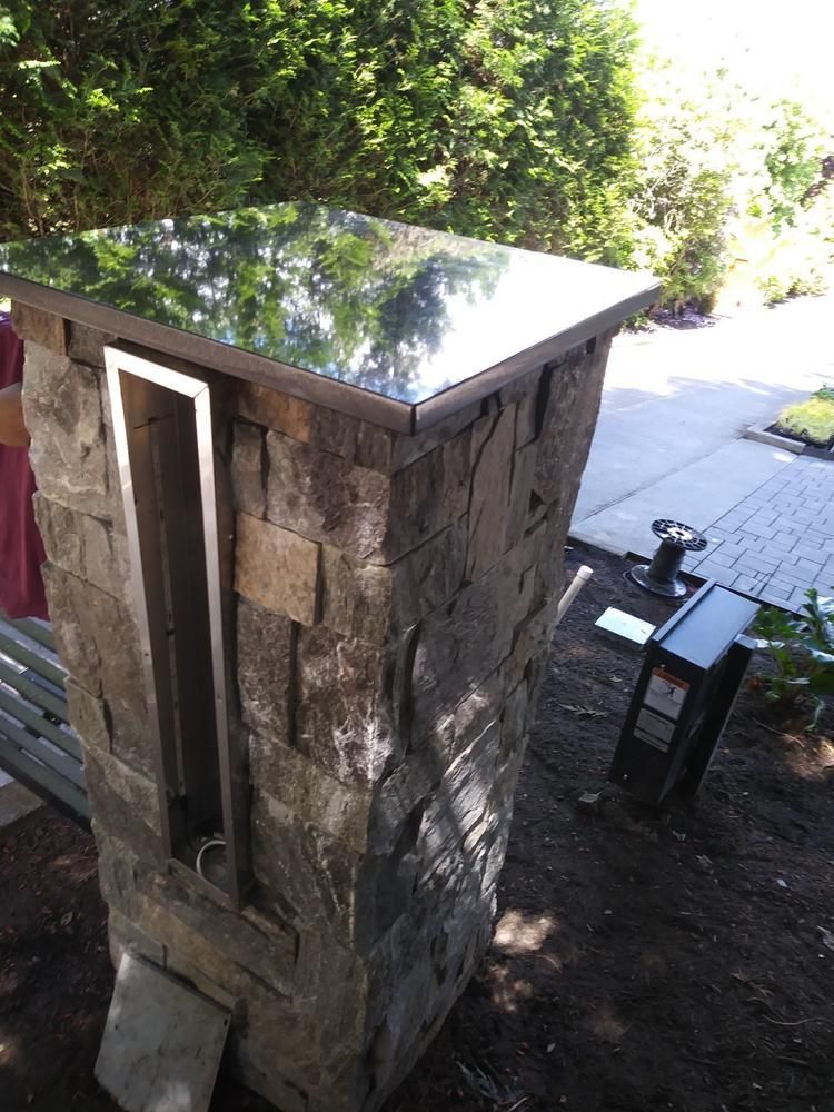 Stone outdoor utility cabinet with metal top beside a patio and bench in a garden