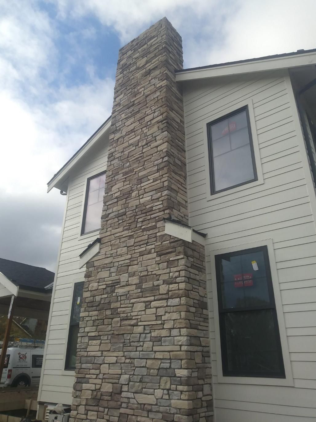 Two-story house with a tall stone chimney and white siding under a cloudy sky