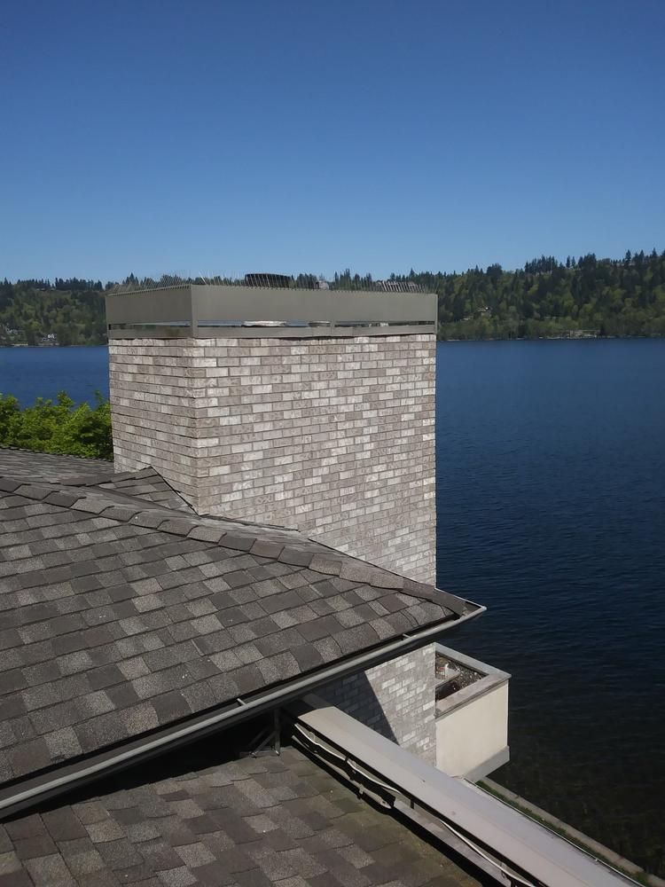 Rooftop and chimney overlooking a calm blue lake with forested shoreline under a clear sky