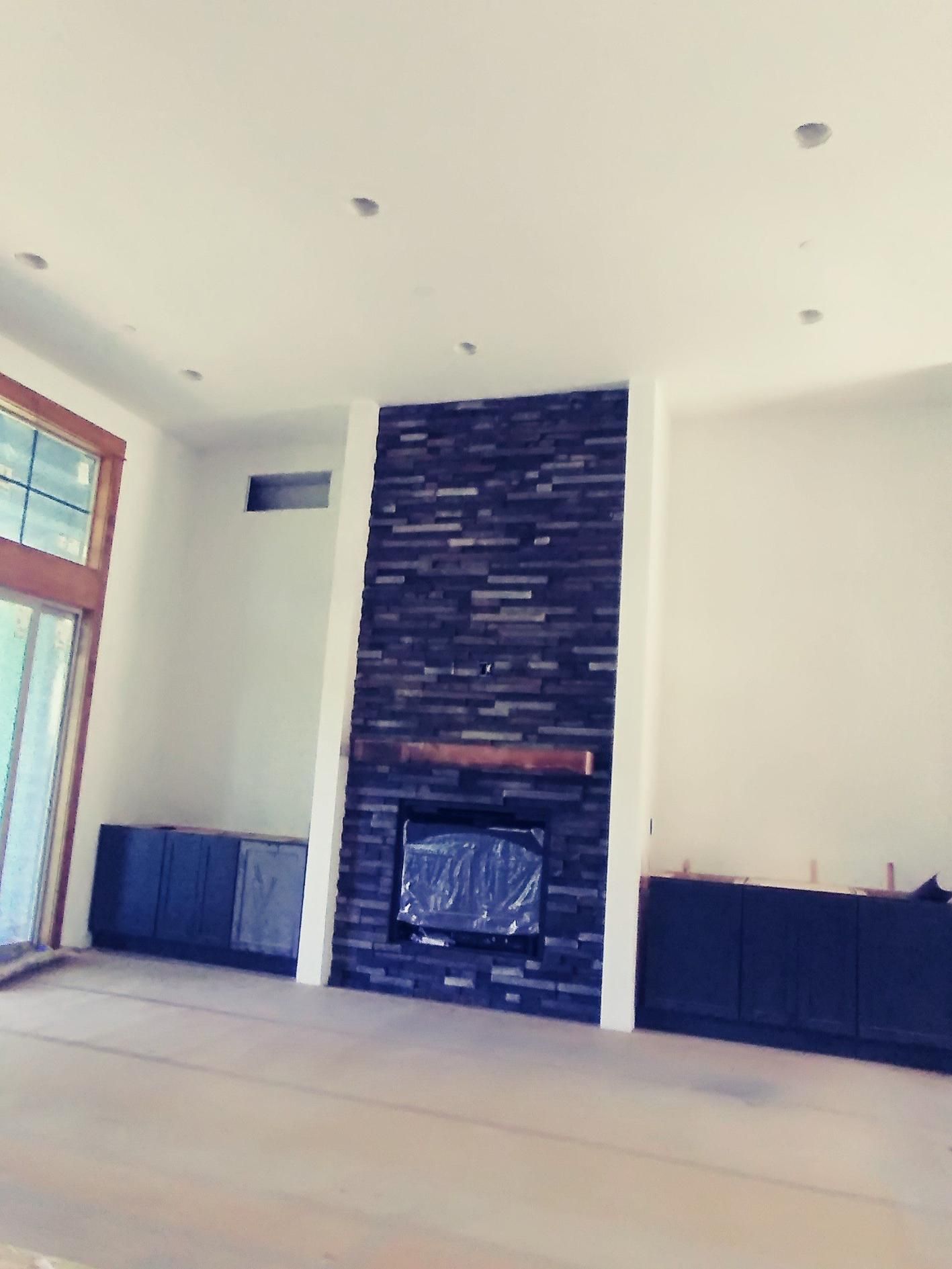 Empty modern living room with white walls, beige floor, and a dark stone fireplace centered on the wall