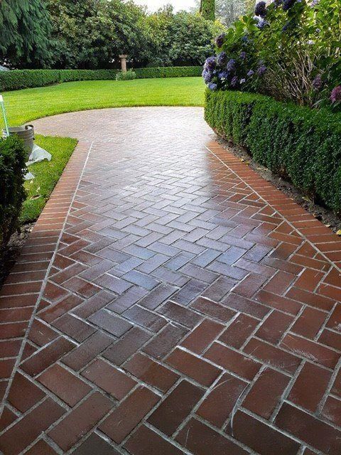 Brick garden path bordered by manicured hedges and purple flowers leading to a lawn