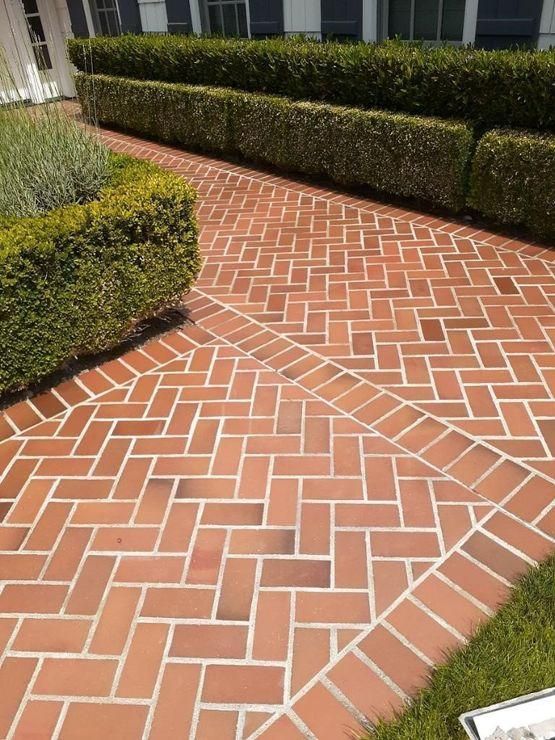 Brick herringbone walkway beside manicured hedges and a small landscaped garden path