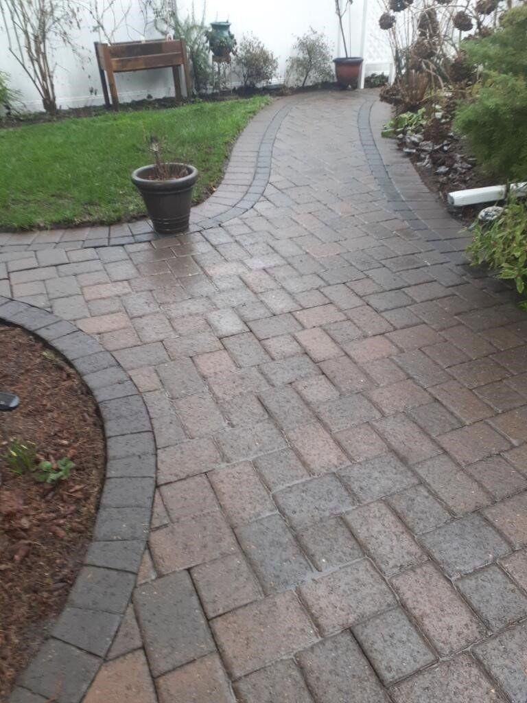 Brick garden pathway curving through a grassy yard with potted plants and shrubs on either side