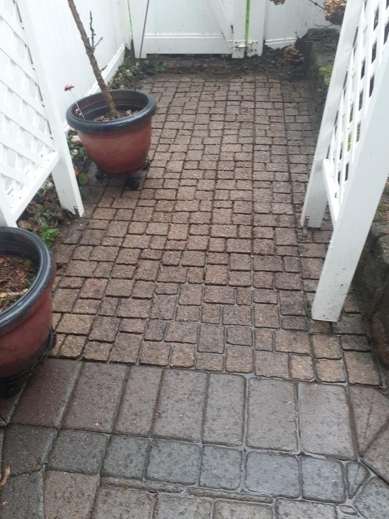 Narrow brick-paved patio walkway between white lattice fences with potted plants along the sides