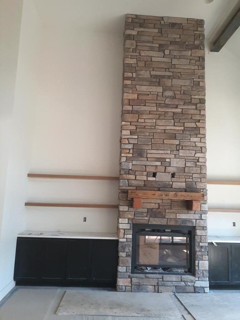 Living room wall with tall stone fireplace, black cabinets, and two wooden shelves