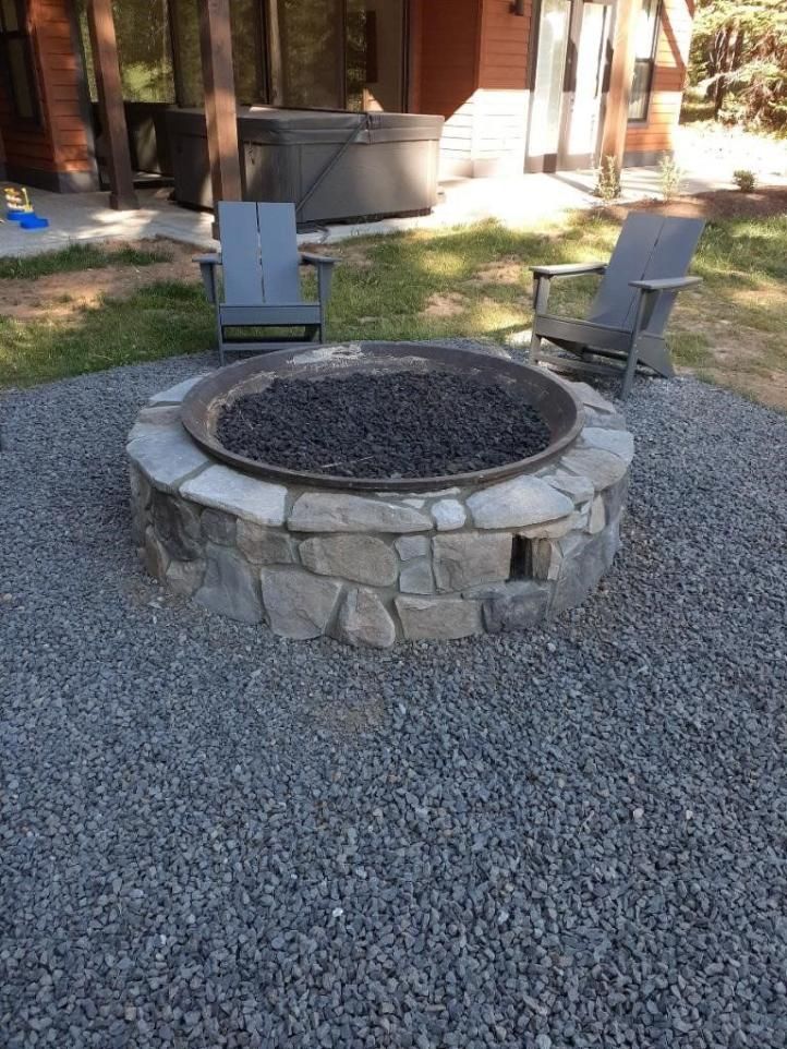 Stone fire pit with two chairs on a gravel patio outside a building