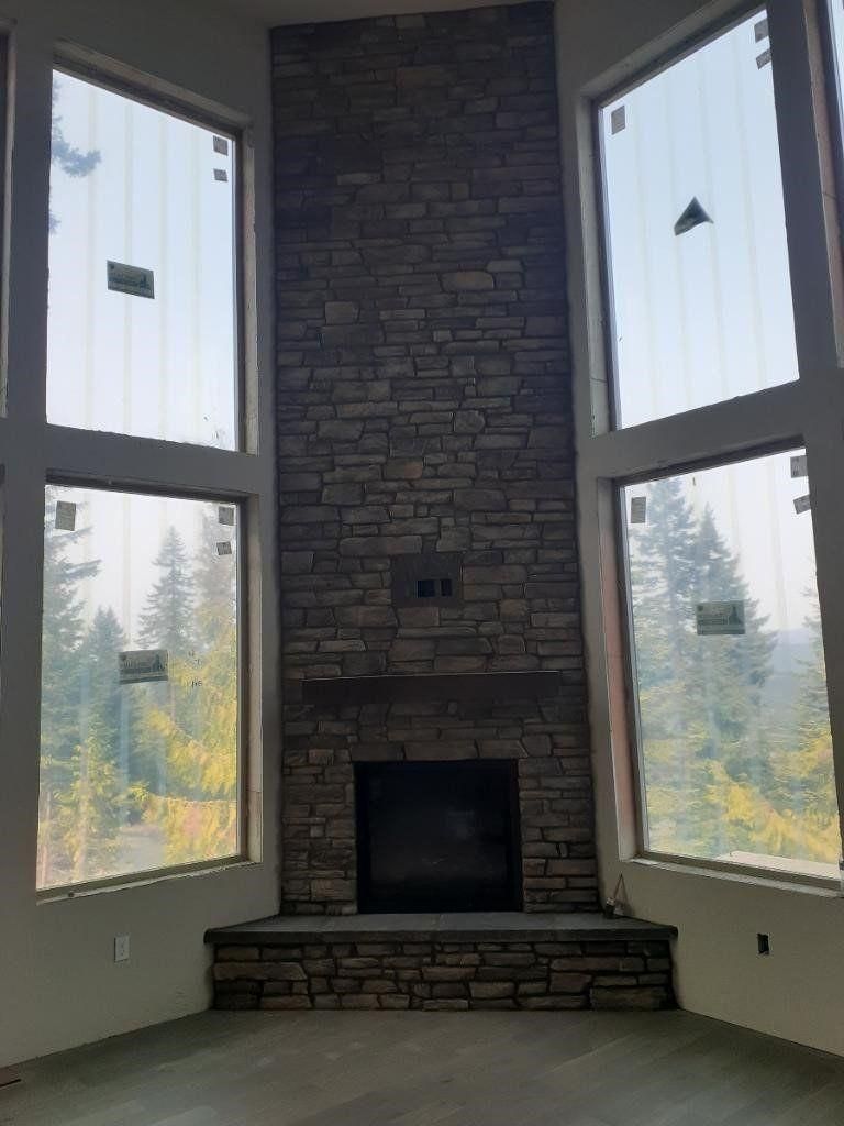 Living room with tall windows, stone fireplace, and a raised hearth overlooking trees outside