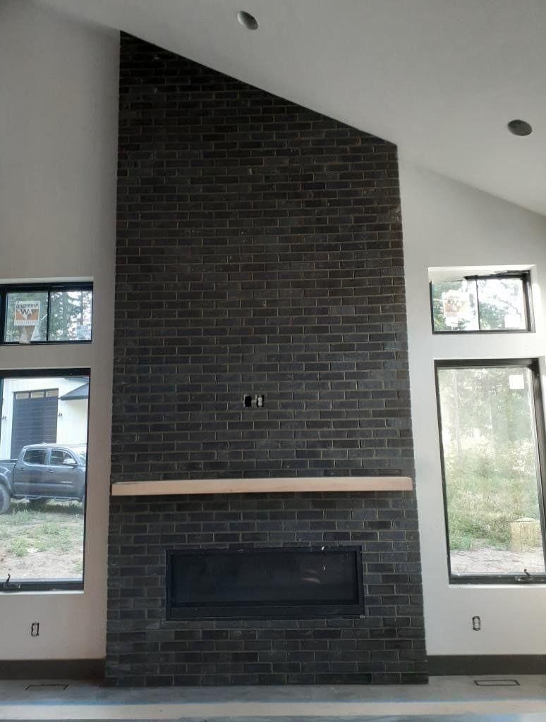 Modern living room fireplace with dark brick, light mantel, and tall windows on both sides.