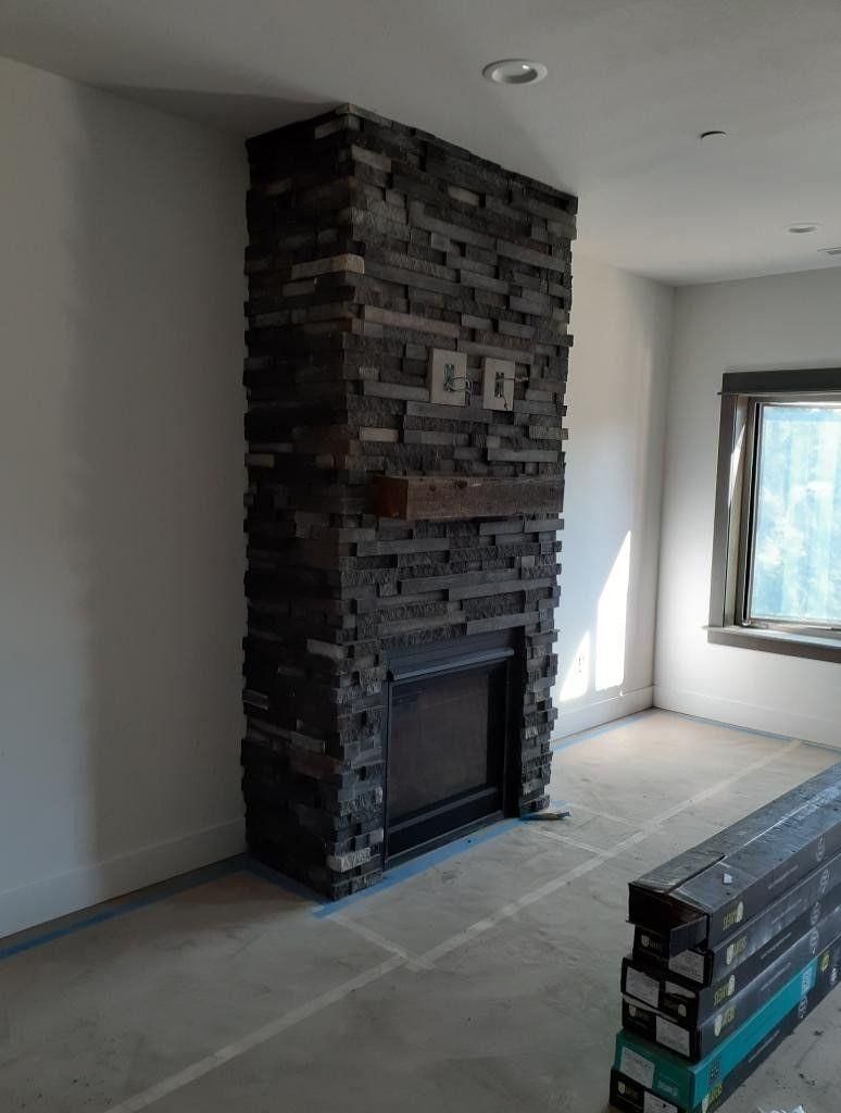 Living room with a stacked-stone fireplace and unfinished floor, with a window on the right.