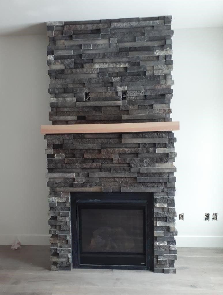 Stacked-stone fireplace with a black glass firebox and light wood mantel in a white room