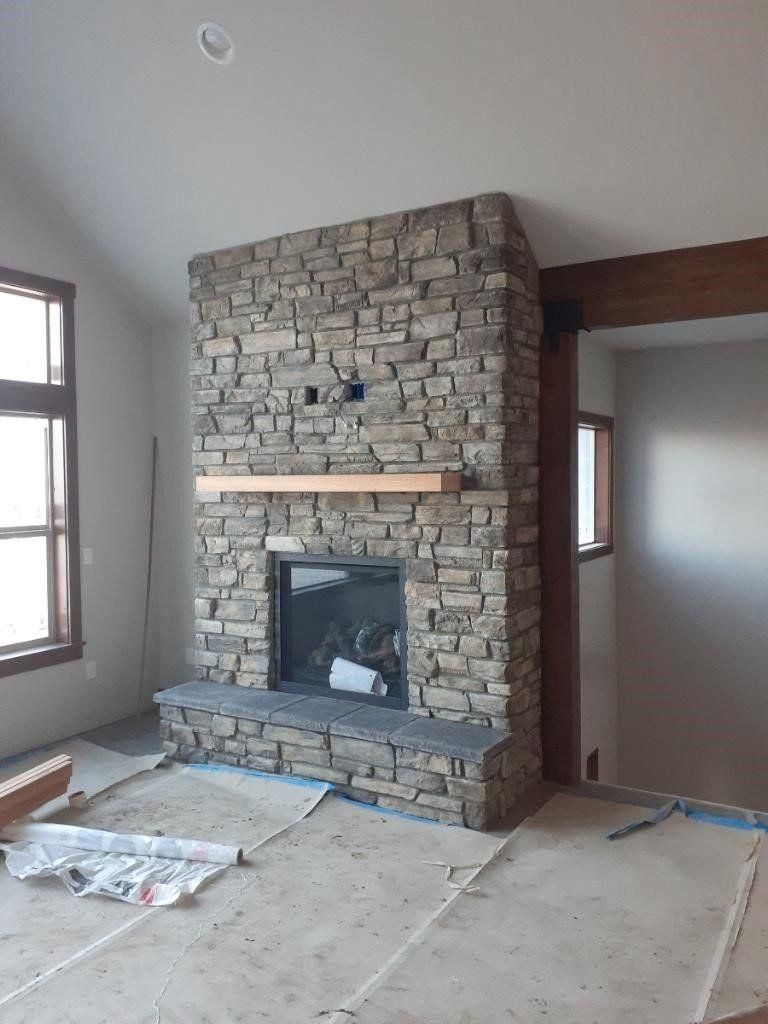 Unfinished room with a stone fireplace and large windows, construction materials on the floor.