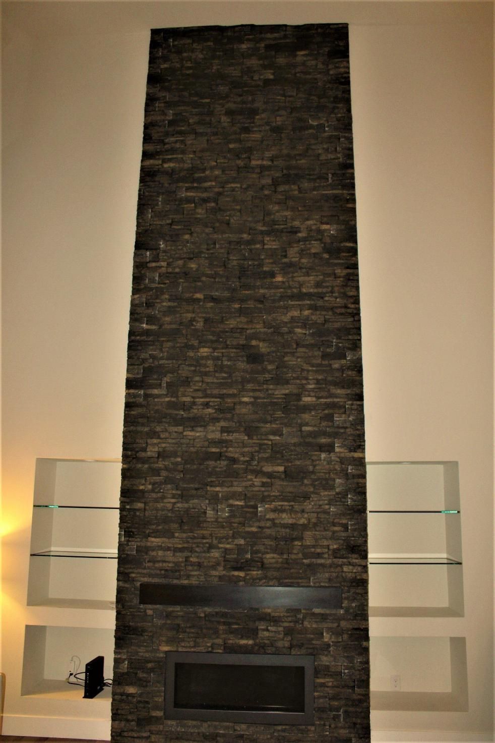 Tall dark stone fireplace with glass shelves on both sides in a warmly lit room